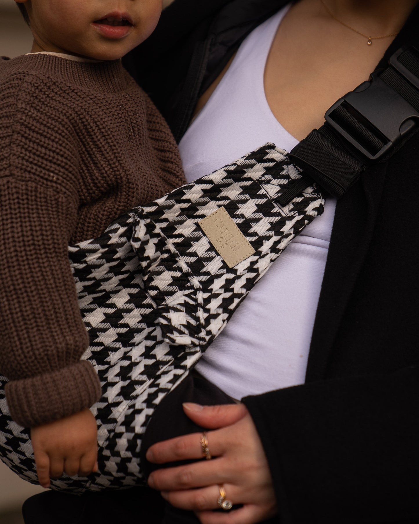 Toddler in a houndstooth-patterned Cuddl.bub toddler carrier held by an adult