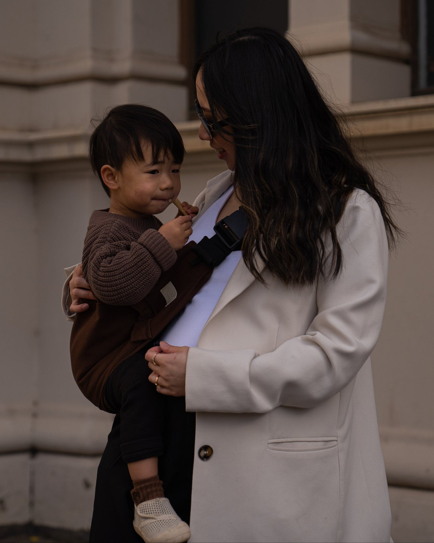 Parent holding toddler in a brown toddler carrier/toddler sling