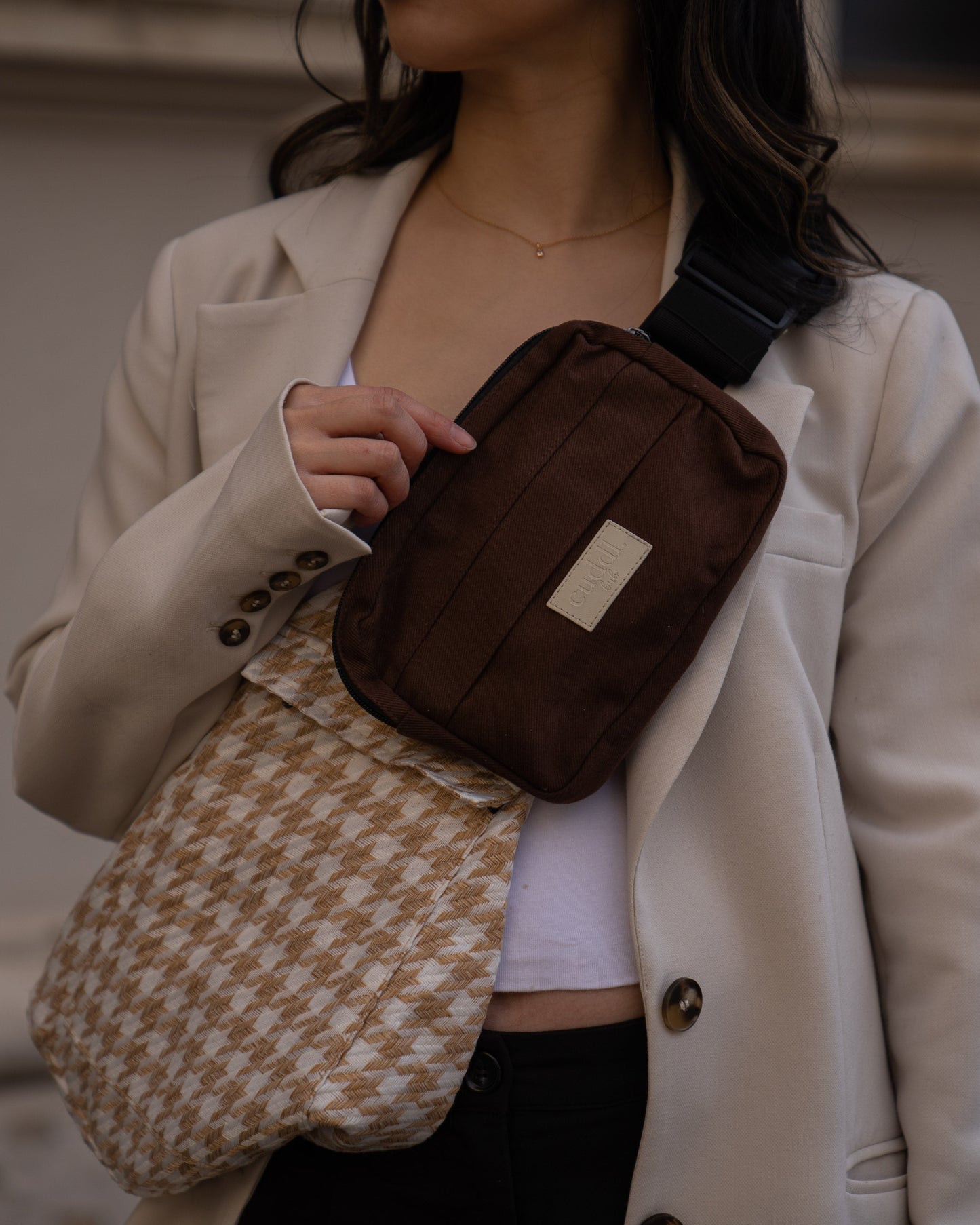 Parent wearing a beige blazer with a Cuddl.bub beige houndstooth-patterned Toddler Carrier/toddler sling and a brown crossbody bag.
