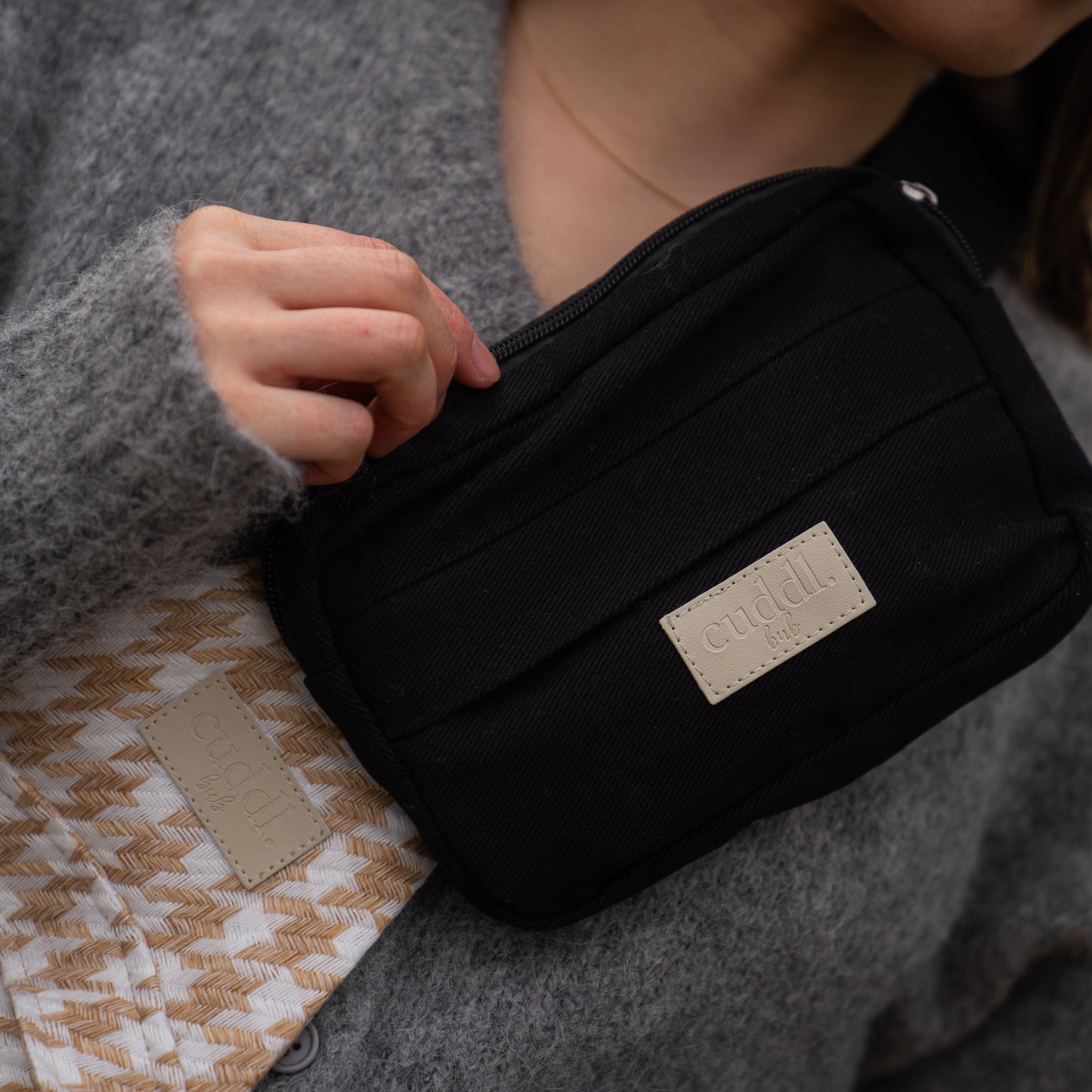 toddler parent wearing a beige houndstooth toddler carrier/toddler sling with a black slide on pouch