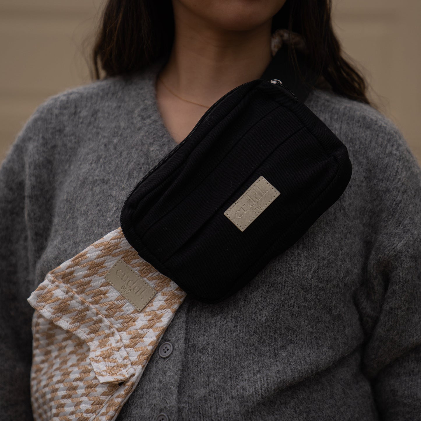 toddler parent wearing a beige houndstooth toddler carrier/toddler sling with a black slide on pouch