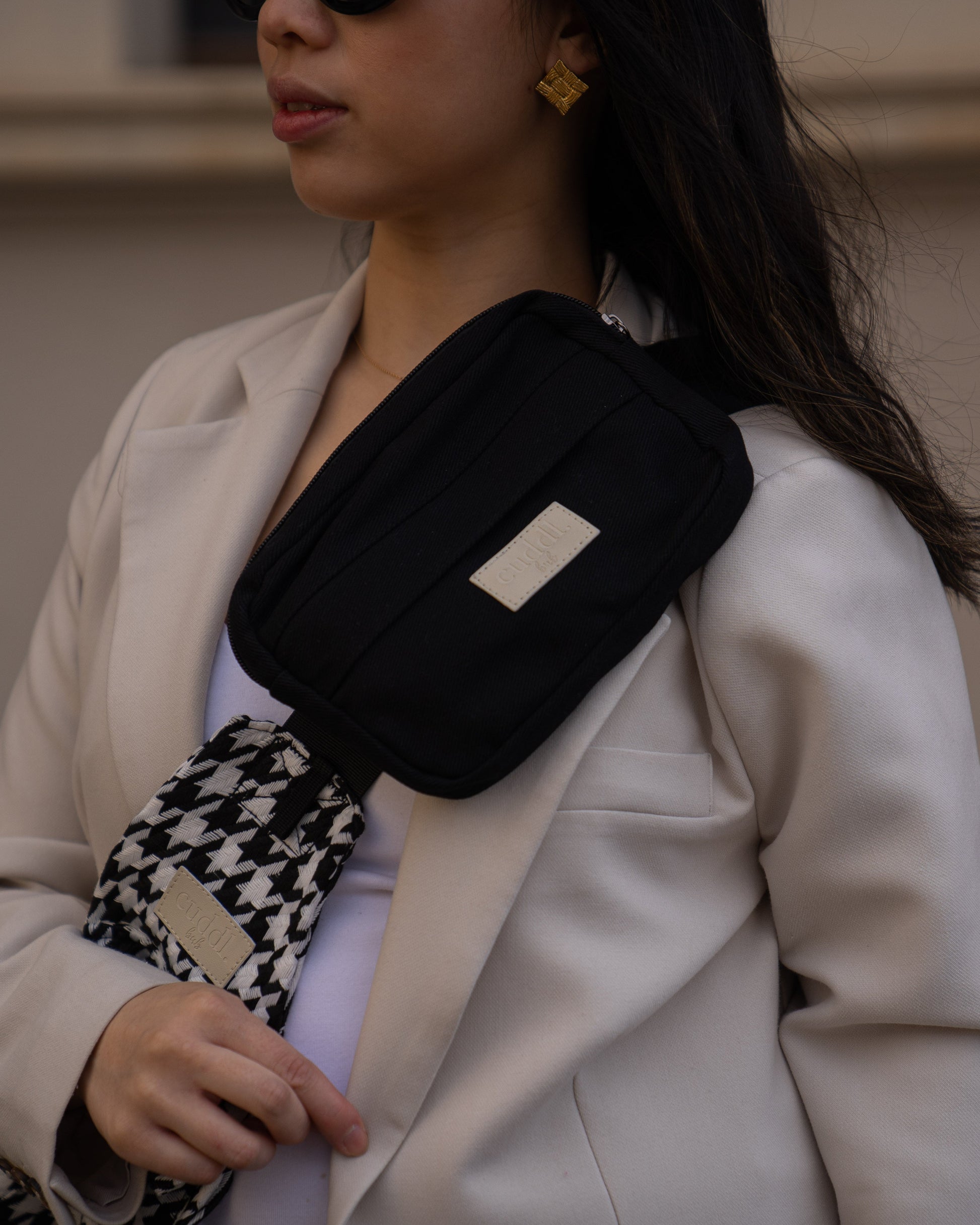 Parent wearing a Cuddl.bub black houndstooth toddler carrier/toddler sling paired with a black crossbody essentials pouch with a blurred background