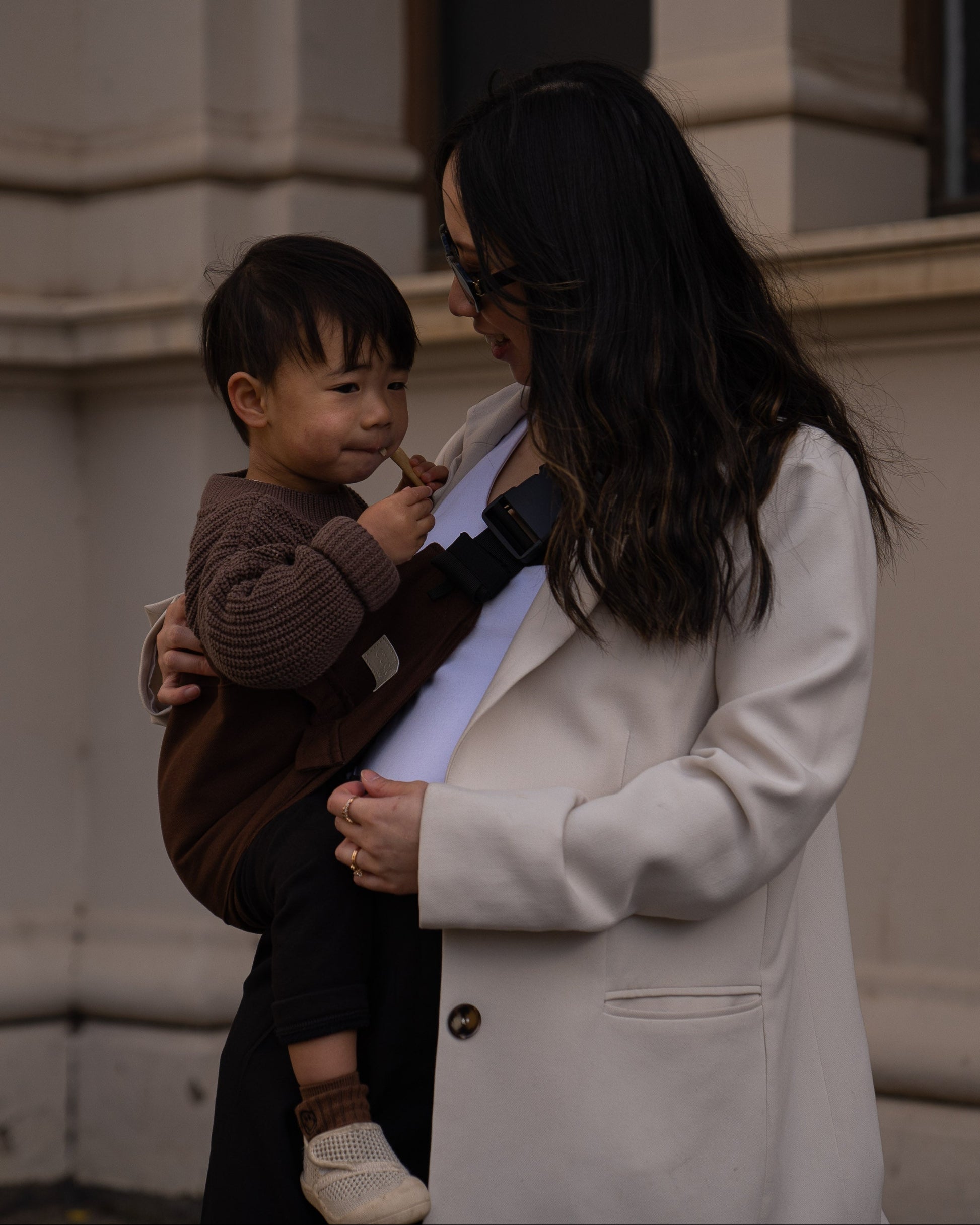 Parent holding toddler in a brown toddler carrier/toddler sling