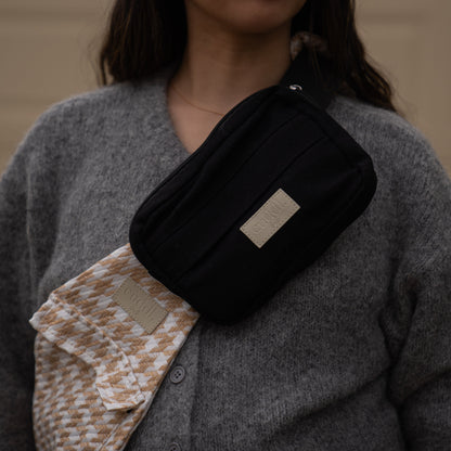 toddler parent wearing a beige houndstooth toddler carrier/toddler sling with a black slide on pouch