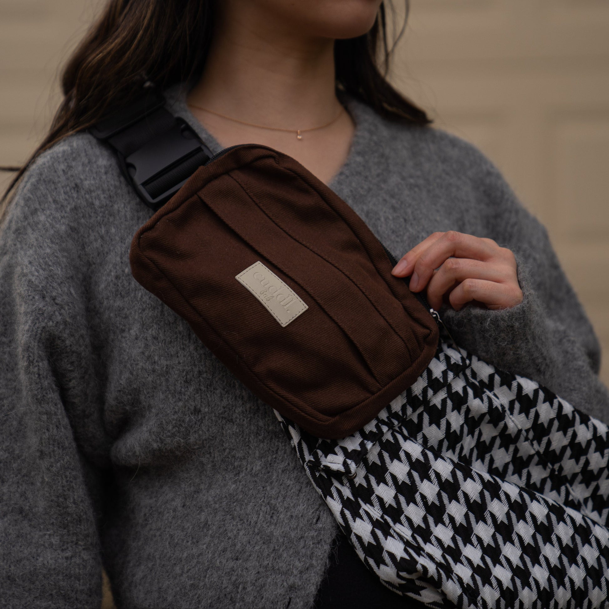 toddler parent wearing a black and white houndstooth toddler carrier/toddler sling with a chocolate brown/cocoa slide on pouch