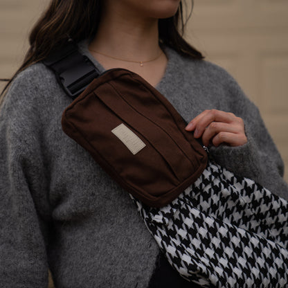 toddler parent wearing a black and white houndstooth toddler carrier/toddler sling with a chocolate brown/cocoa slide on pouch