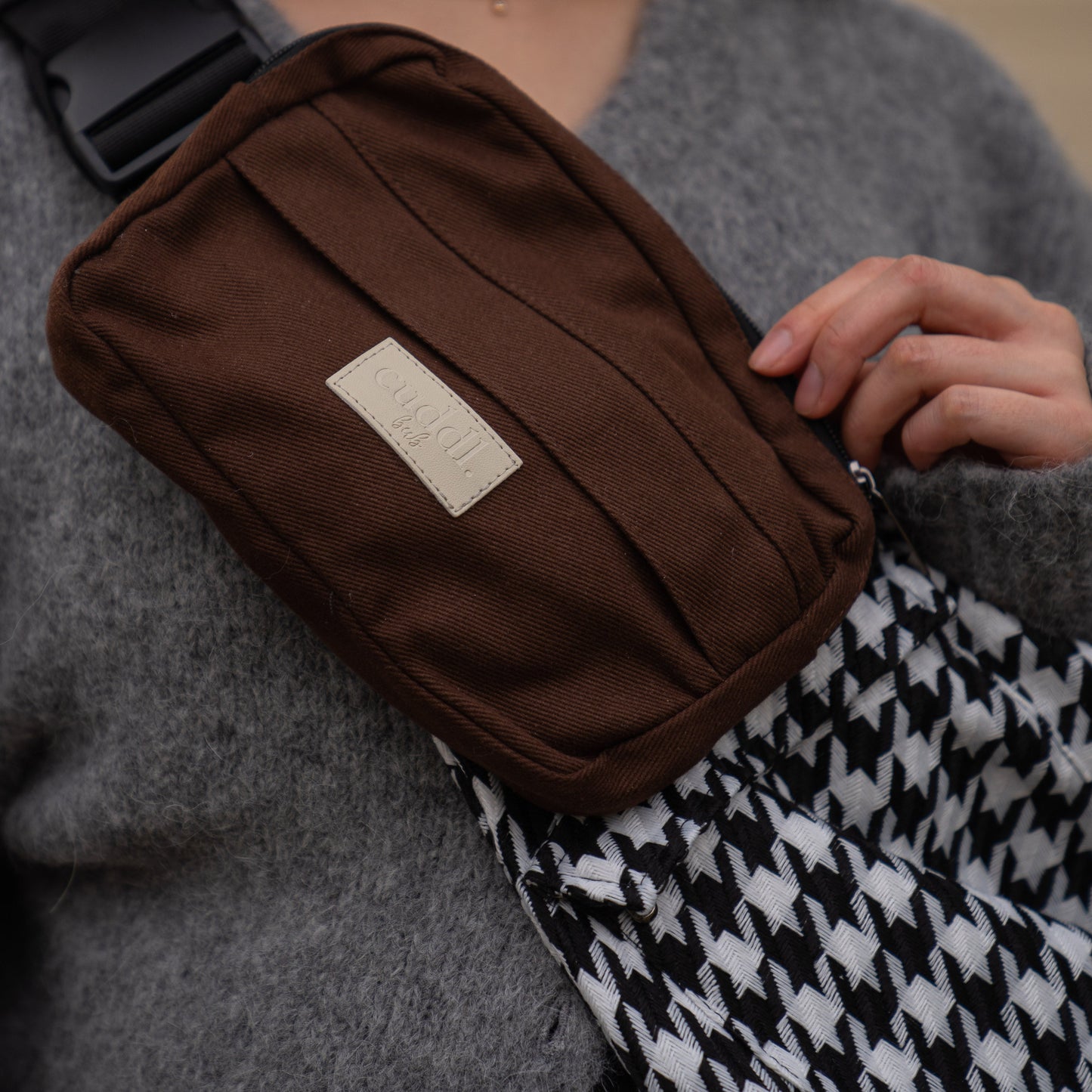 toddler parent wearing a black and white houndstooth toddler carrier/toddler sling with a chocolate brown/cocoa slide on pouch